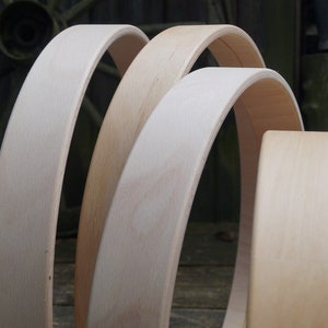 May include: Three unfinished wooden hoops of varying sizes, stacked on top of each other. The hoops are made of light-colored wood and have a smooth, polished finish.