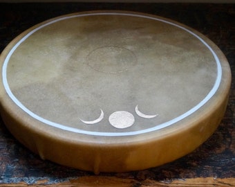 May include: A round, brown leather drum with a white border and gold moon and sun designs.