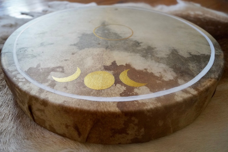 May include: A brown leather drum with a white border and gold crescent moon and sun designs.