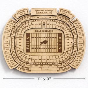 May include: A wooden stadium replica, measuring 28 cm by 23 cm, with detailed laser-cut features. The design includes the words "BILLS SIDELINE" and "BILLS" on the field, with seating sections labeled around the perimeter.
