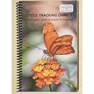 May include: A spiral-bound cycle tracking chart book. The cover shows a butterfly on orange flowers. The interior pages have a chart with columns for cycle tracking. The word "EXAMPLE" is printed across the chart.