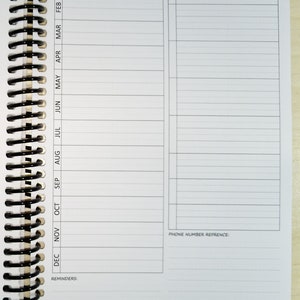 K&ouml;nnte beinhalten: Ein wei&szlig;er Spiralplaner mit Abschnitten f&uuml;r Erinnerungen, Geschenkideen und Telefonnummern. Die linke Seite hat monatliche Spalten von Januar bis Dezember. Oben steht "N&uuml;tzliche Referenznotizen".