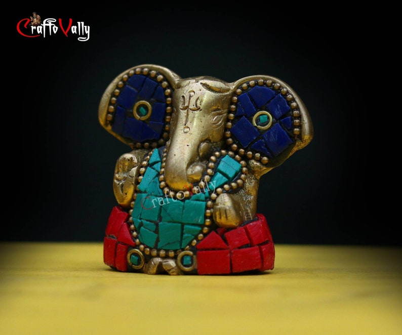 Puede incluir: Una peque&ntilde;a estatua dorada de Ganesha, el dios hind&uacute; de los comienzos, con detalles en mosaico azul y verde. La estatua est&aacute; sentada sobre una base roja y dorada.