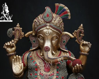 May include: A gold-colored statue of Ganesha, the Hindu god of wisdom and prosperity, with intricate details and colorful gemstones. The statue is adorned with a crown and a beaded necklace.