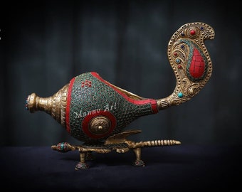 Op de afbeelding: Een decoratieve schelp met ingewikkelde details, met een rood en groen mozaïekontwerp. De schelp is gemonteerd op een gouden standaard met een pauwenachtige staart.
