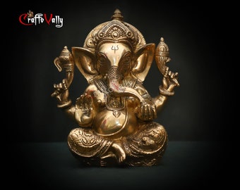 May include: A gold-colored metal statue of Ganesha, a Hindu deity, sitting with his trunk raised and holding a small object in his hand. The statue is decorated with intricate details and has a small mouse at its feet.