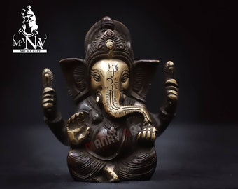 Könnte beinhalten: Eine kleine, dunkelbraune Bronzestatue der hinduistischen Gottheit Ganesha. Die Statue ist aufwendig detailliert, mit goldenen Akzenten im Gesicht und am Rüssel. Ganesha ist sitzend dargestellt, mit der rechten Hand erhoben in einer Geste des Segens und der linken Hand auf dem Knie ruhend. Die Statue steht vor einem schwarzen Hintergrund.