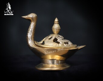 May include: A gold metal incense burner shaped like a swan with an ornate lid. The burner has a round base and a long neck with a detailed design. The lid has a small finial on top.