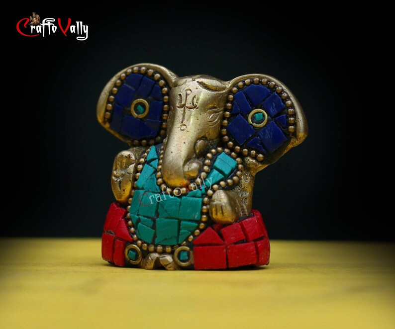 Puede incluir: Una peque&ntilde;a estatua dorada de Ganesha, el dios hind&uacute; de los comienzos, con detalles en mosaico azul y verde. La estatua est&aacute; sentada sobre una base roja y dorada.
