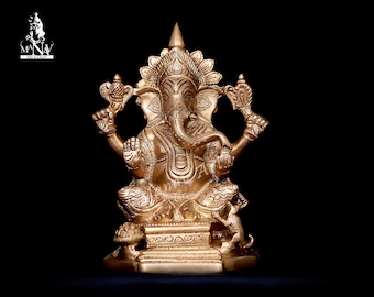 May include: A gold-colored metal statue of the Hindu deity Ganesha. The statue depicts Ganesha sitting on a throne with a mouse at his feet. The statue is intricately detailed and has a traditional design.
