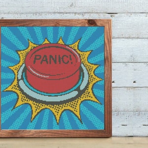 May include: A red button with the word "PANIC!" in white letters, surrounded by a yellow starburst on a blue and white background. The button is framed in a brown wood frame.