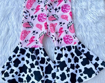 Roze discojurk met cowgirl-belletjes: zwarte wijd uitlopende broek met koeienprint