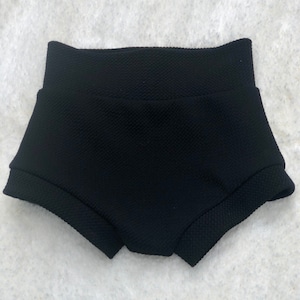 May include: Black high-waisted shorts with a textured, dimpled fabric. The shorts have a wide, folded waistband and a rounded leg opening. The fabric appears to be a stretchy material, suitable for active wear or casual outfits.