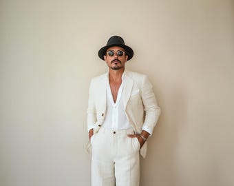 May include: A man wearing a white linen suit with a black hat and sunglasses. The suit has a relaxed fit and a v-neck shirt.