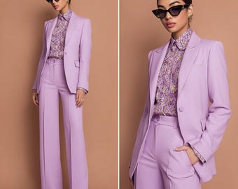 May include: A lavender pantsuit featuring a tailored blazer and wide-leg trousers. The suit is paired with a floral print button-down shirt and black sunglasses. The outfit is a monochromatic ensemble.