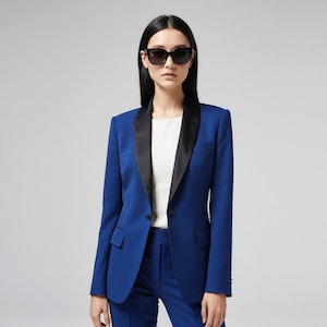 May include: A cobalt blue blazer with a black satin lapel, paired with matching trousers. The blazer features a single-button closure and a tailored fit. The person is wearing black sunglasses and a white top.