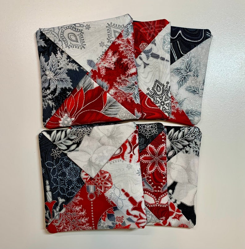 May include: Set of four red, white, and gray fabric coasters with a geometric pattern. The coasters are made of patchwork fabric and have a quilted design.