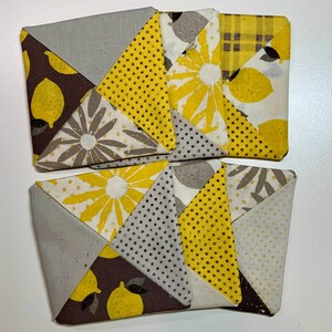 May include: Four handmade fabric coasters with a patchwork design featuring yellow, brown, and gray fabric with lemon and floral patterns.