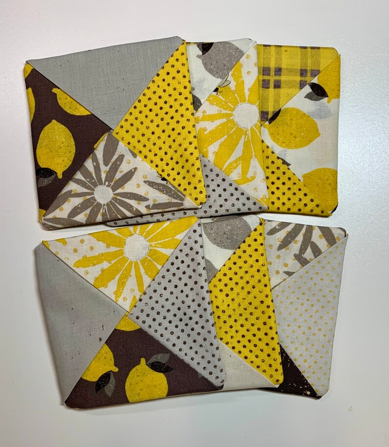 May include: Four handmade fabric coasters with a patchwork design featuring yellow, brown, and gray fabric with lemon and floral patterns.