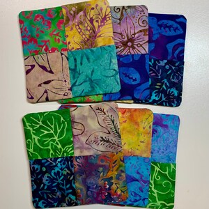 May include: Six handmade fabric coasters with a patchwork design. Each coaster is made of nine squares of different patterned fabric in shades of blue, green, purple, yellow, and brown.