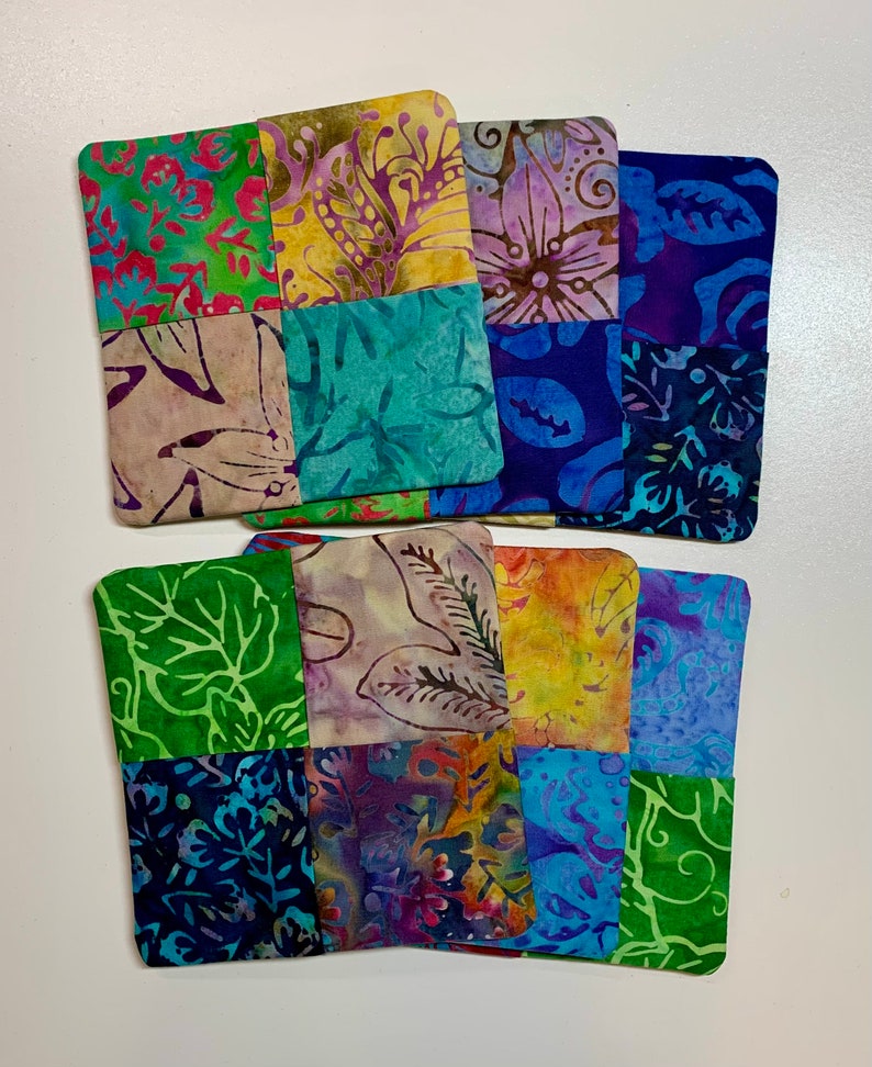 May include: Six handmade fabric coasters with a patchwork design. Each coaster is made of nine squares of different patterned fabric in shades of blue, green, purple, yellow, and brown.
