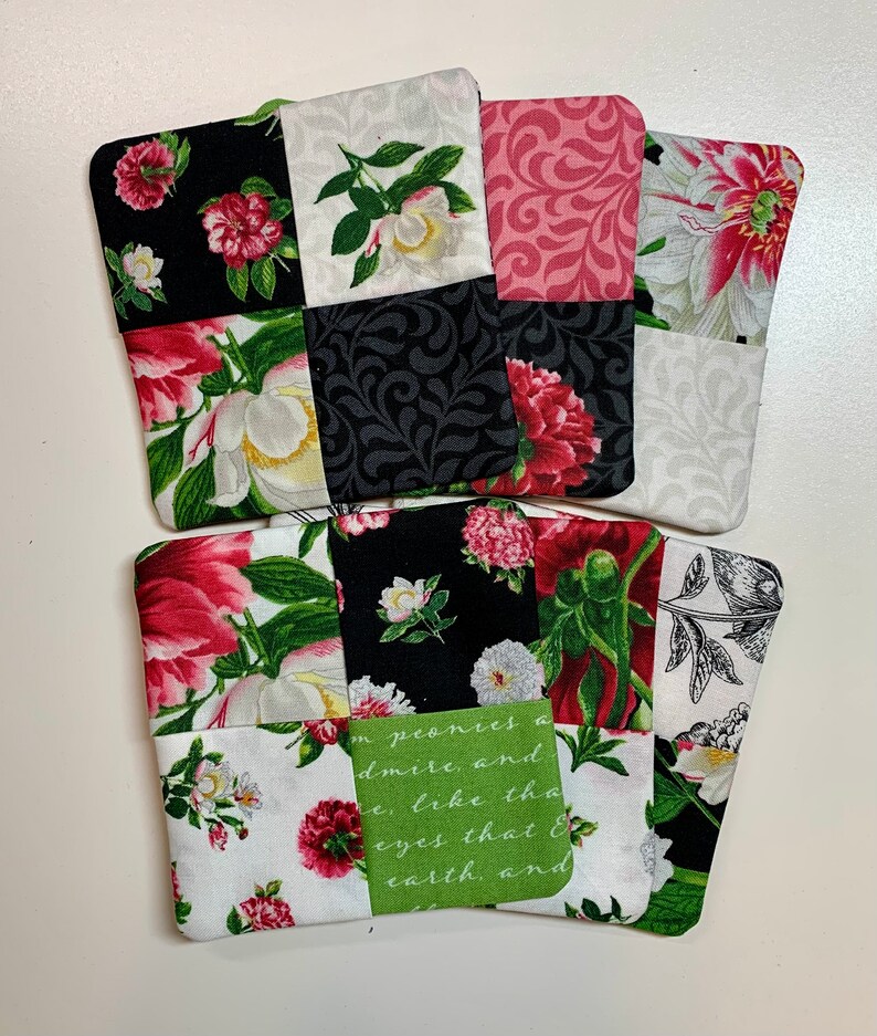 May include: Four square fabric coasters with a patchwork design featuring floral patterns in shades of pink, white, black, and green. The coasters have a quote on one of them that reads "I  peonies a admire, and e, like the eyes that & earth, and"