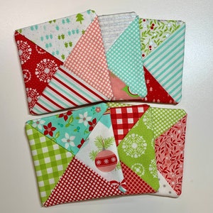 May include: Six handmade fabric coasters with a Christmas theme. The coasters feature a variety of patterns, including red and white polka dots, green and white gingham, and red and white stripes. The coasters are all square and have a pieced design.