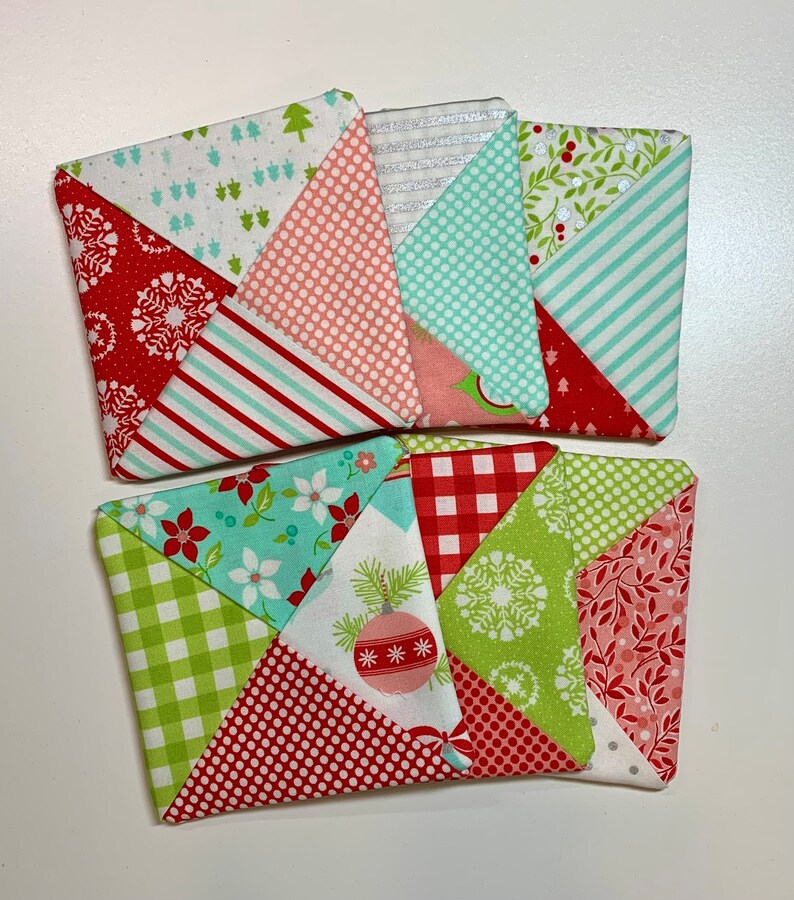 May include: Six handmade fabric coasters with a Christmas theme. The coasters feature a variety of patterns, including red and white polka dots, green and white gingham, and red and white stripes. The coasters are all square and have a pieced design.