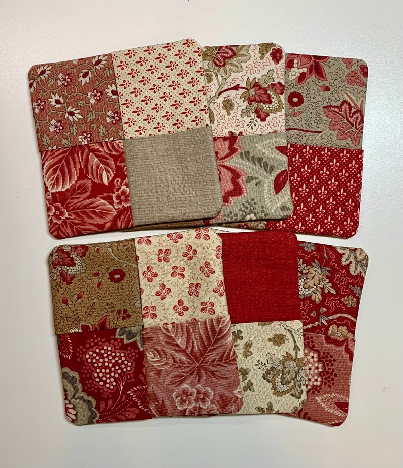 May include: Set of six red and beige fabric coasters with a patchwork design. Each coaster is made of four squares of different patterned fabric.