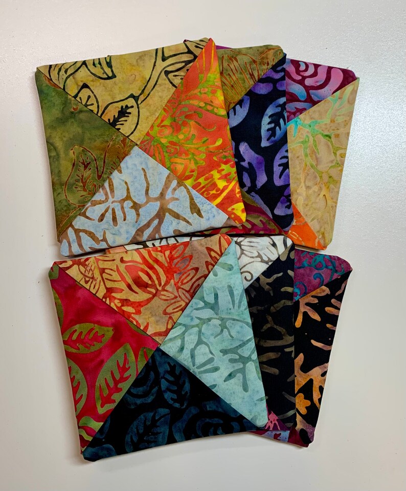 May include: A set of six colorful fabric coasters with a patchwork design featuring various floral patterns. The coasters are made of a soft, textured fabric and are perfect for protecting surfaces from heat and spills.