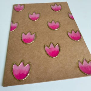 May include: A brown card with a pattern of pink tulip-shaped designs outlined in gold. The tulips have a gradient effect, transitioning from a darker pink at the base to a lighter pink at the top. The card is slightly angled.