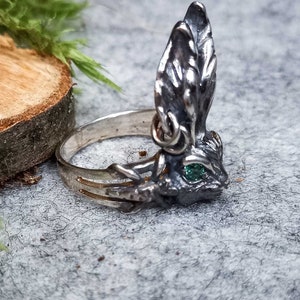 K&ouml;nnte beinhalten: Ein silberner Ring mit einem detaillierten Hasendesign. Der Hase hat einen gr&uuml;nen Edelstein f&uuml;r ein Auge und seine Ohren sind aufgestellt.