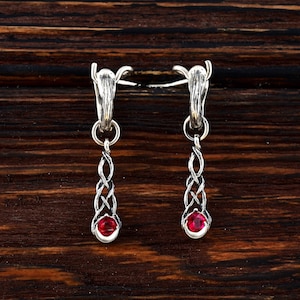 May include: A pair of silver earrings with a dangling design. Each earring features a twisted silver wire with a small red gemstone at the bottom.