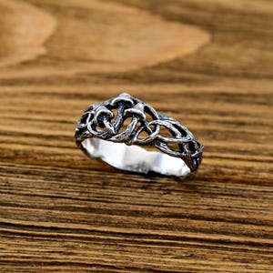 May include: A silver ring with a detailed design of mushrooms and vines. The ring is on a wooden surface.