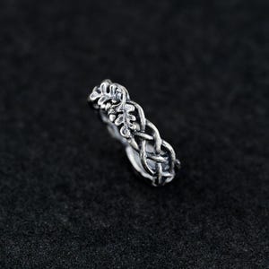 May include: A silver ring with a braided design featuring a leaf pattern. The ring is a delicate piece of jewelry with a nature-inspired design.
