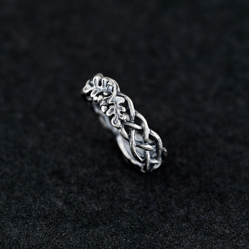 May include: A silver ring with a braided design featuring a leaf pattern. The ring is a delicate piece of jewelry with a nature-inspired design.