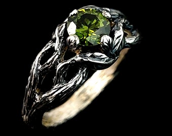 May include: A silver ring with a green gemstone set in a tree branch design.