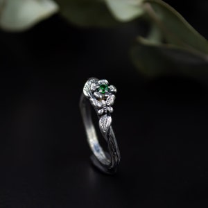 May include: A silver ring with a delicate floral design and a green gemstone. The ring is set on a black background.