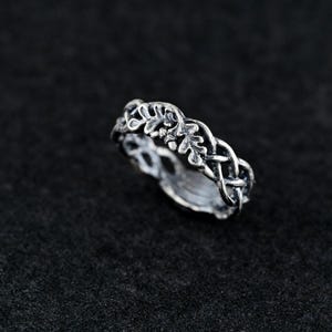 May include: A silver ring with a delicate design of intertwined leaves and branches. The ring is a simple and elegant piece of jewelry.