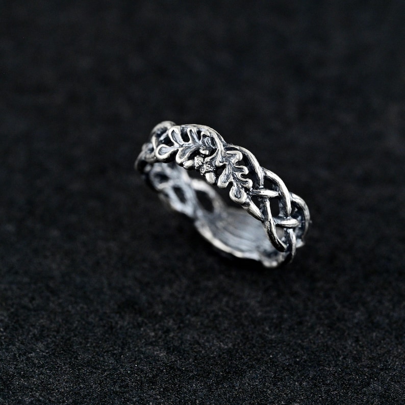 May include: A silver ring with a delicate design of intertwined leaves and branches. The ring is a simple and elegant piece of jewelry.
