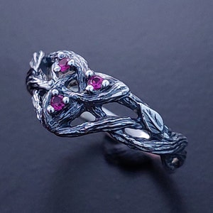 Pode incluir: Um anel de prata com um design de ramo torcido e três pedras preciosas cor-de-rosa.
