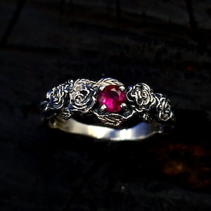 May include: A silver ring with a ruby gemstone surrounded by sculpted roses.