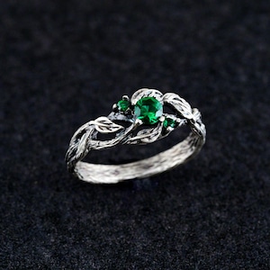 May include: A silver ring with a green gemstone and leaf details. The ring is designed to look like a branch with leaves.