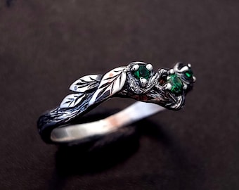 May include: A silver ring with a twig design and three green gemstones. The ring is designed to look like a branch with leaves.