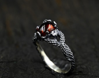 May include: A silver ring with a dark red gemstone set in a twisted, branch-like design.