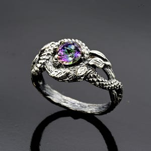 May include: A silver ring with a large, iridescent gemstone set in a detailed, leafy design.