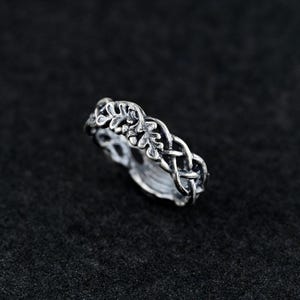 May include: A silver ring with a braided design featuring a leaf motif. The ring is made of metal and has a polished finish.