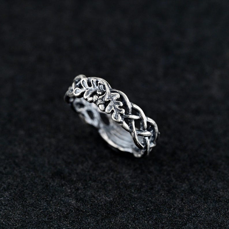 May include: A silver ring with a braided design featuring a leaf motif. The ring is made of metal and has a polished finish.