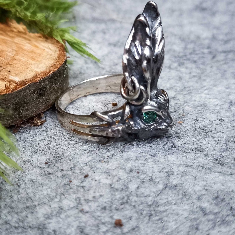 K&ouml;nnte beinhalten: Ein silberner Ring mit einem detaillierten Hasendesign. Der Hase hat einen gr&uuml;nen Edelstein f&uuml;r ein Auge und seine Ohren sind aufgestellt.
