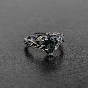 May include: A silver ring with a dark green gemstone set in a twisted branch design.